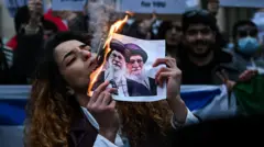 Seorang demonstran anti-rezim Iran menyalakan rokok dengan kertas yang menyala bergambar Ali Khamenei, Pemimpin Tertinggi Iran, saat berkumpul di luar Konsulat AS di Milan, pada 13 Januari 2026