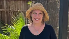 Sierra Hanson usa uma blusa preta e um chapéu. Atrás dela há plantas e uma cerca