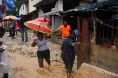 Haiti'nin başkenti Port-Au-Prince'te bir adamın elinden tutan şemsiyeli bir kadın sel suyunun içinden yürüyor 