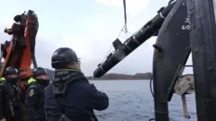 ヘルメットをかぶった3人が船上で「SG-1ファゾム」グライダーを海へ投下している。滑車によって持ち上げられ、水中に降ろされている