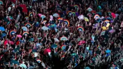 Público do show de lady gaga com leques com cores do arco-íris