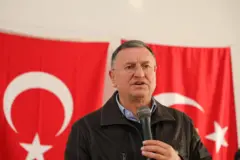 Lütfü Savaş iki Türkiye bayrağının önünde mikrofona konuşuyor. 