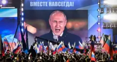 Putin berbicara di depan kerumunan massa di Moskow, dengan kalimat "Bersama, Selamanya" terpampang di atas layar.