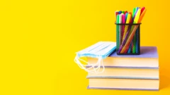 Pila de libros con mascarilla y marcadores.