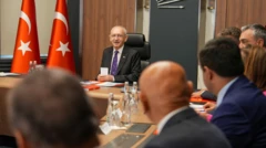 Kemal Kılıçdaroğlu iki Türk bayrağının yanında masa başında oturuyor. Arkadan gördüğümüz kafalar ona bakıyor.