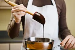 Fotografia colorida mostra uma pessoa branca levantando uma espátula com chocolate derretidorocco gallo slotuma panela