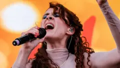 Kate Nash cantando no palco com um fundo laranja