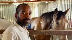 Khaled stands in front of horse in stable