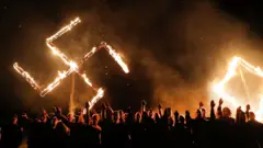 Simpatizantes del niazismo con una esvástica de fuego al fondo