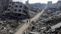 صورة تظهر أشخاصاً يمشون وسط دمار واسع في منطقة سكنية على إثر العمليات العسكرية الإسرائيلية في منطقة جباليا شمالي قطاع غزة 