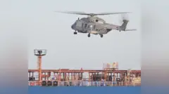 灰色のヘリコプター1機が、赤色の石油タンカーの上を飛んでいる