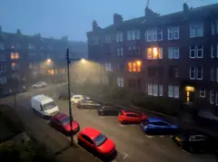 Una foto de una calle brumosa de Glasgow, con varios carros estacionados.