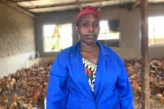 Clémence Murekatete yambaye itaburiya y'ubururu ahagaze mu nzu y'inkoko ze