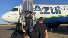 Passageiros embarcando em avião da companhia aérea Azul num dia de céu sem nuvens