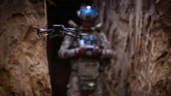 На переднем плане дрон, на заднем, размытом, упарвляющий им военный.