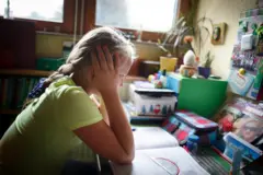 Uma criança com cadernos abertos e olhando com aspecto frustrado