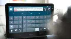 Uma imagem em close de uma tela de computador com um teclado digital, que Sarah usa para construir palavras usando a tecnologia do olhar. A tela diz: "Sinto-me eu mesma novamente usando o Grid 3 da Smartbox com minha voz do Eleven Labs e não pareço uma..."
