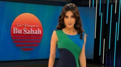 Ela Rümeysa Cebeci'nin dar elbiseli bir stüdyo pozu. Arkasında El Rumeysa ile bu sabah yazıyor