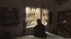 Pessoa sentada em uma cama olhando para a janela