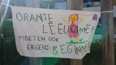 A banner reads "Orange Lionesses must also start somewhere" at the De Buut primary school playground