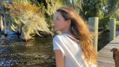 A modelo Gisele Bündchen está sentada em um píer contemplando a paisagem