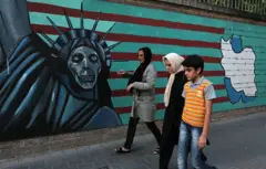 Uma família iraniana caminha ao lado de grafites anti-americanos no muro da antiga embaixada dos EUA em Teerã. Foto de 2015.