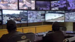 Dos hombres observan las imágenes en las pantallas de un centro de vigilancia. 