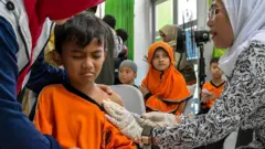 Seorang petugas kesehatan memberikan vaksin campak kepada seorang siswa sekolah dasar selama peluncuran program pemeriksaan kesehatan gratis untuk anak-anak, di Jakarta pada 4 Agustus 2025