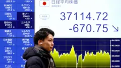 Homem asiático em frente à painel indicando queda nas ações no Japão