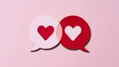 Recorte em papel de dois balões de conversa em forma de coração vermelho, atraídos um pelo outro, sobre fundo rosa