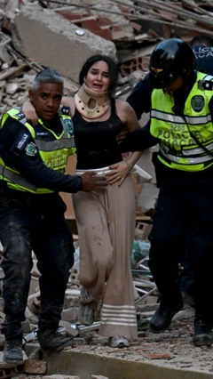 Una mujer con cuello ortopédico está siendo retirada por dos rescatistas de los escombros de un edificio colapsado