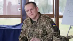 Олександр Півненко у військовій формі сидить у приміщенні на тлі вікна 