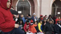 Migrantes, algunos con niños, frente a la iglesia del Sagrado Corazón de El Paso.
