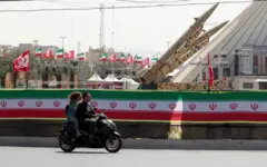 زوجان إيرانيان يركبان دراجة نارية بجوار صواريخ إيرانية من طراز ذوالفقار، معروضة في ساحة آزادي في طهران، إيران، 24 يوليو 2026