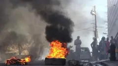 Varios hombres detrás de unos neumáticos en llamas en Puerto Príncipe.