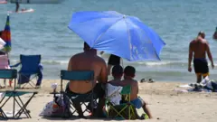People sit under an umbrella at a beach in France in June