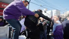 Milei é evacuado de um comício na província de Buenos Aires, depois que manifestantes atiraram pedras. Observa-se o segurança ajudando o presidente argentino a sair de uma caminhonete branca.