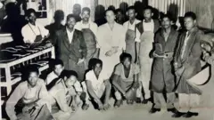ኬጋን አስላንያን ከሸዋ ጫማ ፋብሪካ ሠራተኞች ጋር በፋብሪካው ውስጥ ከማሽኖቹ ጋር የቡድን ፎቶግራፍ 1965