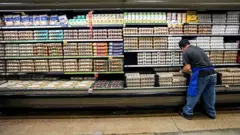 Pessoa de costas examina bandejas de ovos em setor refrigerado de supermercado