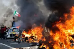 Un manifestante sostiene una bandera mexicana mientras se incendian autos en una calle de Los Ángeles el domingo.