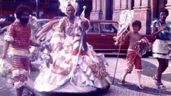 Foto de Carnaval de 1975 em que Eduardo Simão Pinto se reconheceu ao ver no Instagram, com um casal de porta bandeiras, um menino sem camisa e outros carnavalescos na rua.