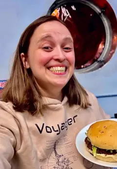 Rebeca segurando um prato com um hambúrguer e sorrindo