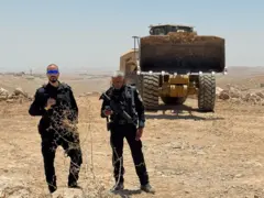 ከስካቫተር ፊት ለፊት ቆሙ ሁለት የእስራኤል ፖሊሶች