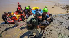 Rescuers carry a man from a dinghy beached on a muddy bank