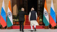 Putin and Modi walk together, their backs to the camera, a Russian and an Indian flag on either side. They are heading into a building with a red carpet.