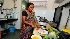 A woman wearing a printed saree chops vegetables on a kitchen counter in Delhi 