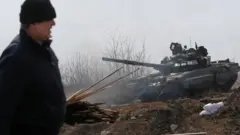 Umugabo ugenda iruhande rw'igifaru cy'ingabo zishyigikiye Uburusiya mu ntambara ya Ukraine n'Uburusiya, aha ni mu nkengero y'umujyi wo mu majyepfo ya Ukraine uri ku cyambu uri mu gihirahiro wa Mariupol, ku itariki ya 20 y'ukwezi kwa gatatu mu 2022