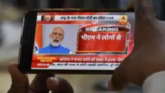 জাতির উদ্দেশ্যে প্রধানমন্ত্রী মোদীর দেওয়া ভাষণ দেখছেন মাস্ক পরিহিত এক ব্যক্তি।