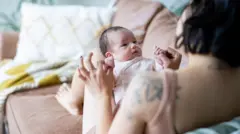 Bebê de poucas semanas sentado no colo da mãe sobre um sofá