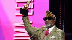 Koffi Olomide azamuye igihembo, nyuma yo guhabwa igihembo cy’umunyabigwi cya AFRIMA, mu birori byo gutanga ibihembo by’umuziki bya All Africa Music Awards, kuri hoteli ya Eko Hotels, mu gace ka Victoria Island, i Lagos muri Nigeria, ku itariki ya 21 Ugushyingo (11) mu 2021. 